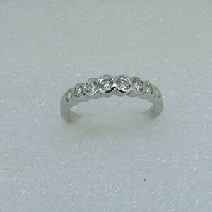 May include: A silver band ring with a row of small round clear stones.