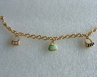 Könnte beinhalten: Ein goldenes Kettenarmband mit drei Anhängern in Form von Handtaschen. Die Anhänger sind mit Emaille in rosa, weiß, grün und schwarzen Streifen verziert.