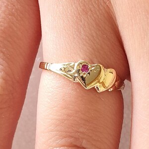 May include: Gold ring featuring two interlocking hearts with a small red gemstone at the centre.