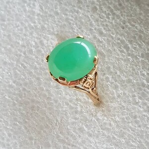 May include: A gold ring with a green oval gemstone set in a delicate filigree design.