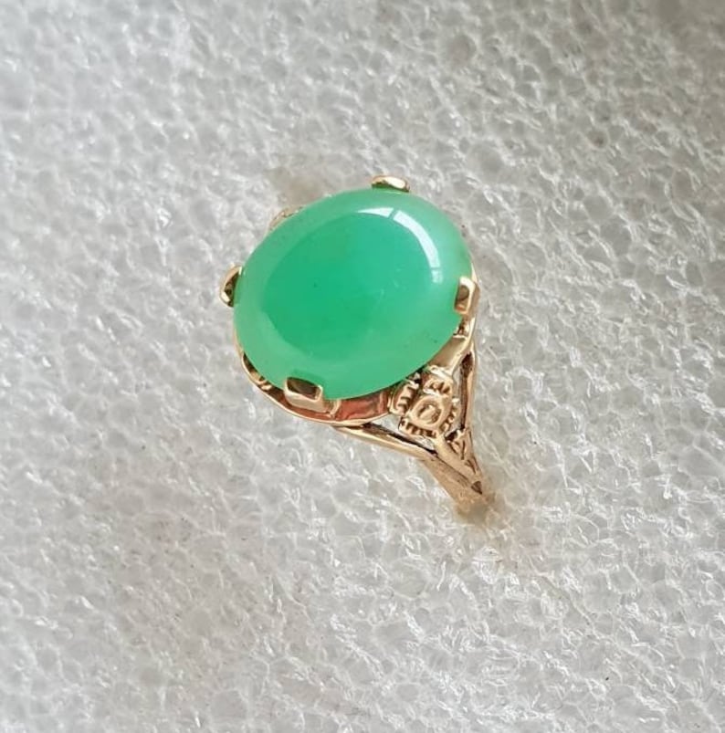May include: A gold ring with a green oval gemstone set in a delicate filigree design.