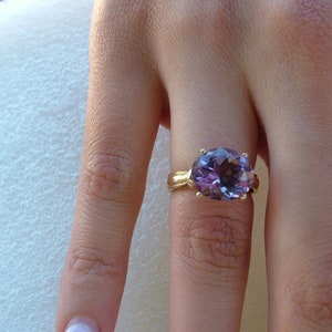 Puede incluir: Un anillo de oro con una gran amatista de forma ovalada. La piedra preciosa es de color morado oscuro y tiene un corte facetado.