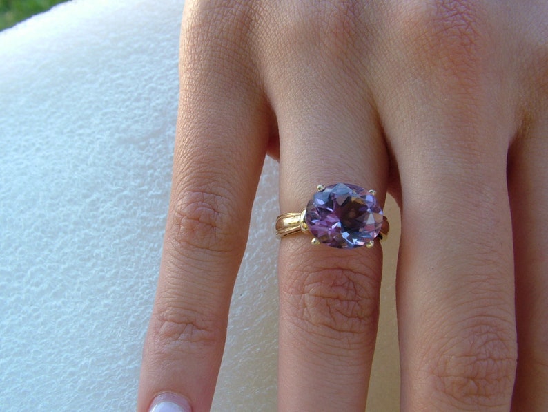 Puede incluir: Un anillo de oro con una gran amatista de forma ovalada. La piedra preciosa es de color morado oscuro y tiene un corte facetado.
