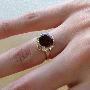 May include: A gold ring with a large, dark red gemstone set in a floral design.