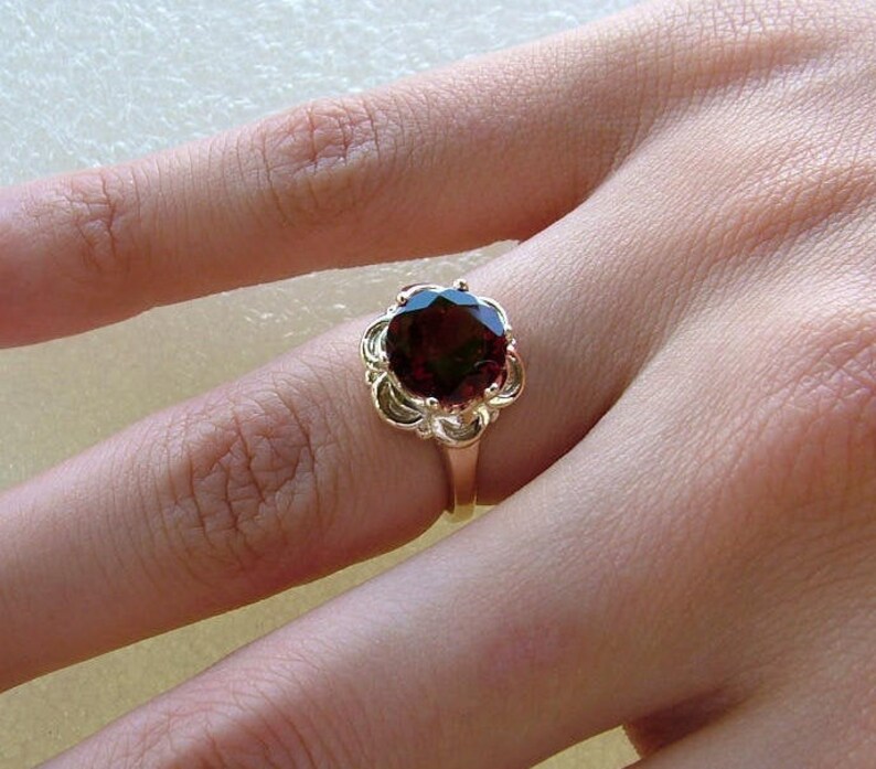 May include: A gold ring with a large, dark red gemstone set in a floral design.