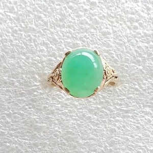 May include: A green gemstone ring with a delicate floral design. The ring is made of silver and features a round, cabochon-cut gemstone.