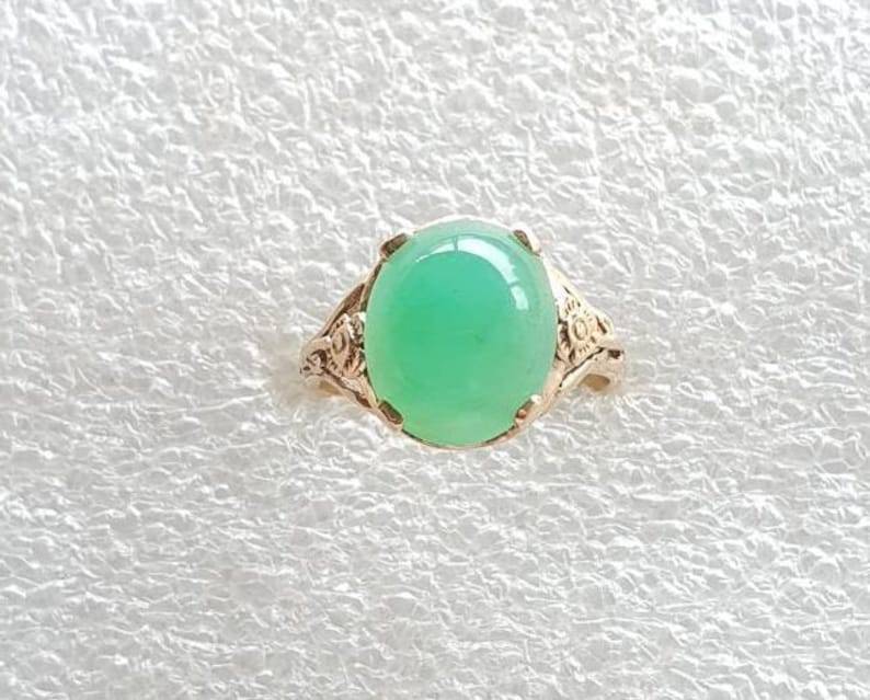 May include: A green gemstone ring with a delicate floral design. The ring is made of silver and features a round, cabochon-cut gemstone.