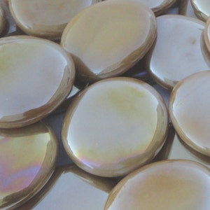 May include: A group of iridescent, round, glass tiles in a light brown color. The tiles are smooth and have a glossy finish.