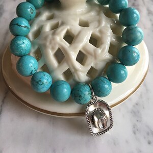 May include: Turquoise gemstone bracelet with a silver cowboy hat charm. The bracelet is made of round beads and is strung on a stretchy cord.