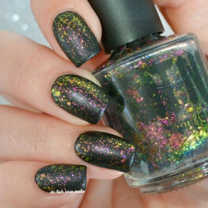 May include: Black nail polish with iridescent green, gold, and pink glitter. The bottle is clear and shows the glitter inside.