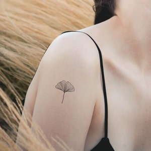 May include: A simple black line drawing of a ginkgo leaf on a person's shoulder.