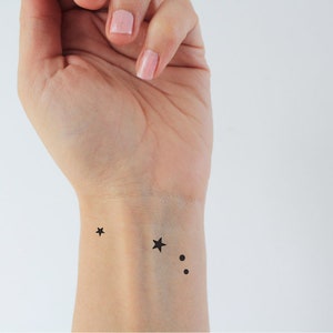 May include: A close-up of a person's wrist with a small black star tattoo and two black dots.