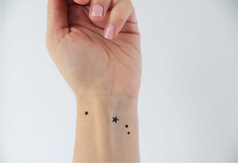 May include: A close-up of a person's wrist with a small black star tattoo and two black dots.