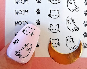 May include: A sheet of nail art stickers with a crescent moon design and multiple black and white cat illustrations. The stickers feature paw prints and the word "Meow" repeated three times. The sheet is on a pink surface and a finger with a pink nail is shown with a cat sticker applied.