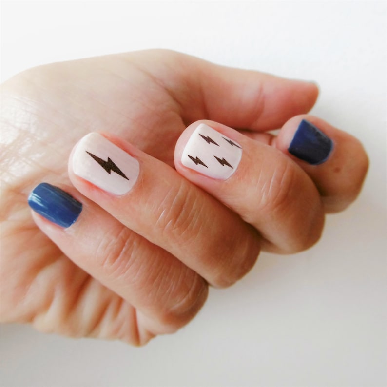 May include: A hand with white nail polish with black lightning bolt designs on the nails. Two of the nails are painted a dark blue color.