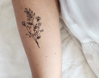 Può includere: Un semplice disegno a linea nera di un bouquet di fiori selvatici sul braccio di una persona.