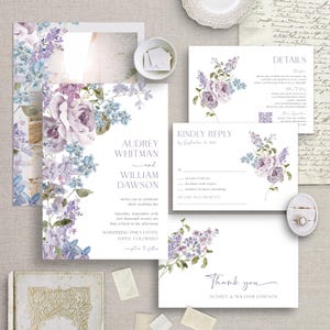 May include: A collection of wedding stationery featuring floral designs in shades of purple and blue. The invitation includes the names "Audrey Whitman and William Dawson" and event details. Other cards include "Kindly Reply" and "Thank you."