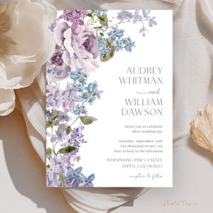 Puede incluir: Una invitación de boda con elementos florales en acuarela en tonos morados y azules. La invitación incluye los nombres "Audrey Whitman y William Dawson" y detalles del evento. El diseño es elegante y romántico.