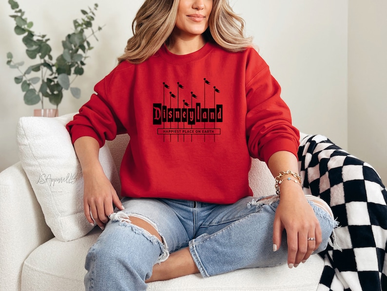 May include: A red sweatshirt with a black graphic of the Disneyland sign with the text "Happiest Place on Earth".