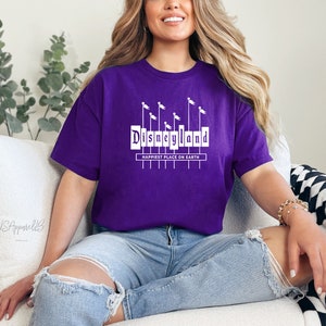 May include: Purple t-shirt with a white graphic of the Disneyland sign with the text "Happiest Place on Earth".