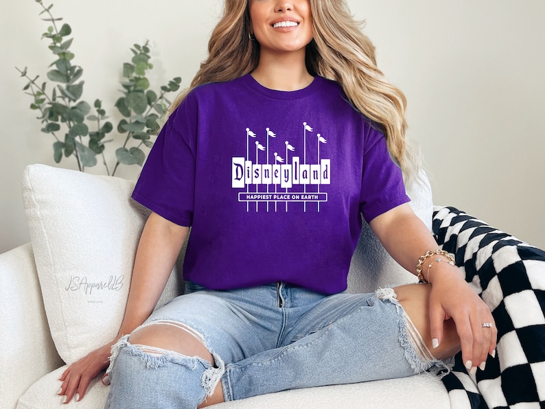 May include: Purple t-shirt with a white graphic of the Disneyland sign with the text "Happiest Place on Earth".