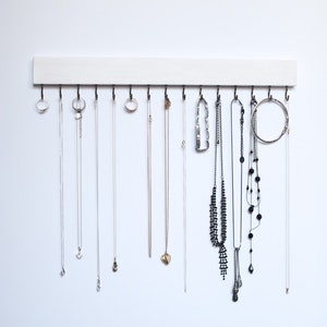 May include: A white wooden jewelry organizer with hooks for hanging necklaces and bracelets. The organizer has a simple design and is perfect for storing and displaying jewelry.