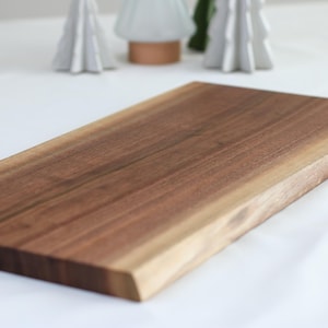 May include: A large, rectangular wooden serving board made of walnut wood. The board has a natural, live edge finish and is perfect for serving cheese, charcuterie, or other appetizers.