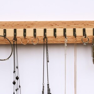 May include: A wooden jewelry organizer with 10 hooks for hanging necklaces, bracelets, and earrings. The organizer is made of light brown wood with a natural grain pattern.