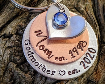 Puede incluir: Llavero de capas de plata y cobre con un dije de corazón con una piedra de cristal azul. El llavero dice "Mom est. 1998 Godmother est. 2020".