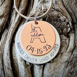 May include: A silver and copper key chain with the letter A and the name Addison engraved on the copper side. The silver side reads "Wanted. Chosen. Loved. Adopted." and includes the date "04.15.23".