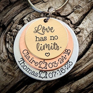 May include: A silver, copper, and gold layered keychain with the inscription "Love has no limits."  The bottom layer also includes the names "Thomas" and "Claire" and the dates "07.16.23" and "03.24.18".
