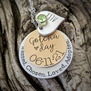 May include: Silver necklace with a heart charm engraved with "ALLY" and a round charm with the text "Gotcha day 06.11.21 Wanted. Chosen. Loved. Adopted."