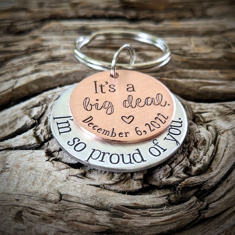 Puede incluir: Un llavero de plata y cobre con el texto "It's a big deal. December 6, 2011. I'm so proud of you."