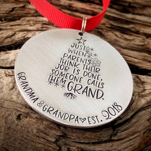 May include: A silver Christmas ornament with a tree design and the text "JUST WHEN PARENTS THINK THEIR JOB IS DONE, SOMEONE CALLS THEM GRAND. GRANDMA & GRANDPA EST. 2018"