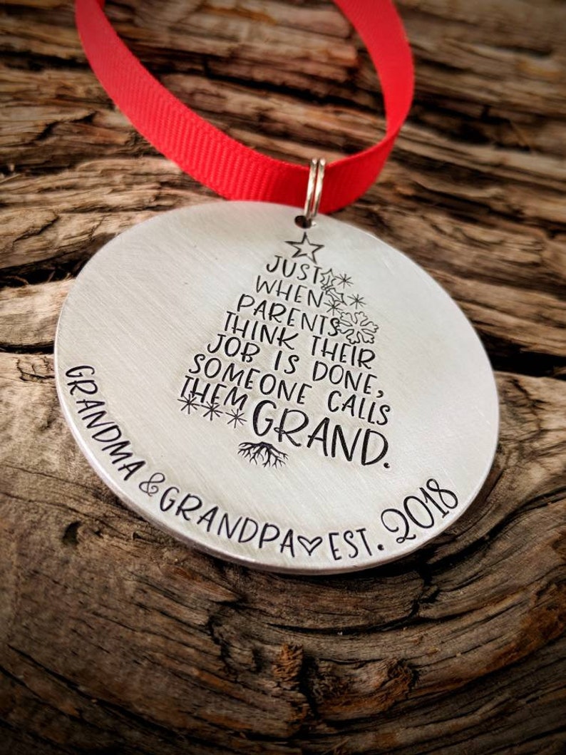 May include: A silver Christmas ornament with a tree design and the text "JUST WHEN PARENTS THINK THEIR JOB IS DONE, SOMEONE CALLS THEM GRAND. GRANDMA & GRANDPA EST. 2018"