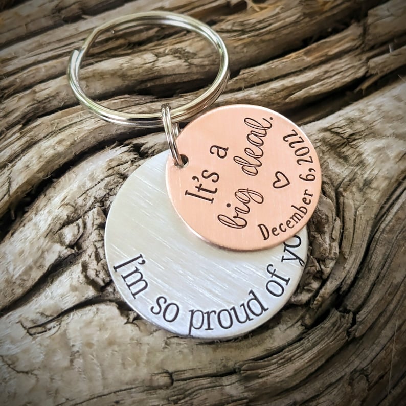 Puede incluir: Un llavero de plata y cobre con el texto "It's a big deal" en el lado de cobre y "I'm so proud of you" en el lado de plata. El lado de cobre tambi&eacute;n incluye un coraz&oacute;n y la fecha "December 6, 2021".