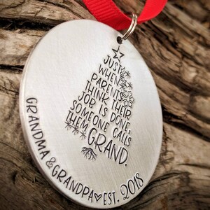 May include: A silver Christmas ornament with the text "Just when parents think their job is done, someone calls them Grand. Grandma & Grandpa Est. 2018" engraved on it.