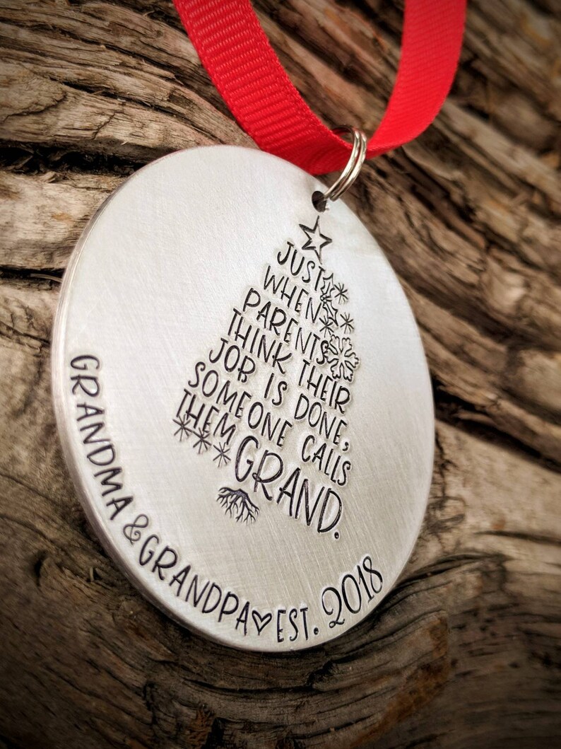 May include: A silver Christmas ornament with the text "Just when parents think their job is done, someone calls them Grand. Grandma & Grandpa Est. 2018" engraved on it.