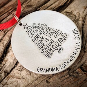 May include: A silver Christmas ornament with a tree design and the text "Just when parents think their job is done, someone calls them Grand."  The ornament also includes the text "Grandma & Grandpa Est. 2010".
