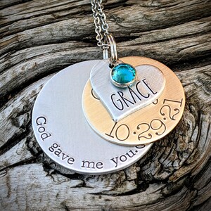 May include: Silver necklace with two round pendants. The top pendant is a heart with the name "GRACE" and the date "10.29.21" engraved on it. The bottom pendant has the text "God gave me you." A turquoise gemstone is set in the heart pendant.