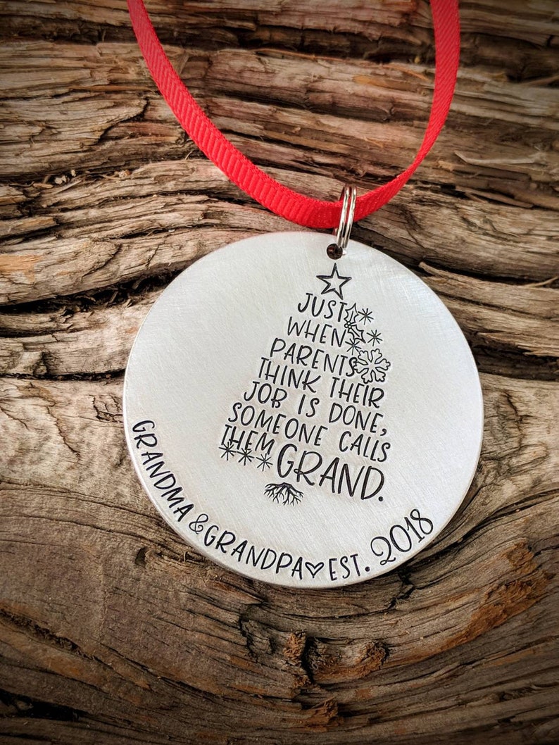 May include: Silver Christmas ornament shaped like a Christmas tree with the text "Just when parents think their job is done, someone calls them Grand." and "Grandma & Grandpa Est. 2018" at the bottom.