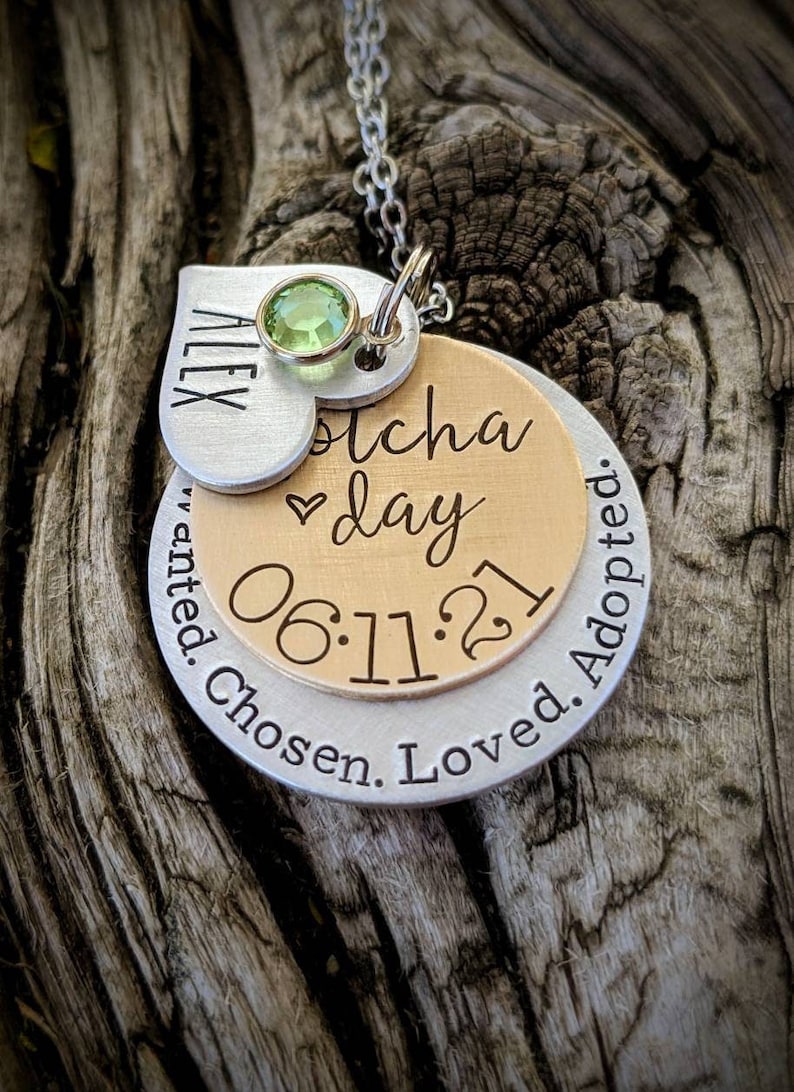 May include: Silver heart charm necklace with a green gemstone, a gold circle charm with the text "Gotcha day 06.11.21" and a silver circle charm with the text "Wanted. Chosen. Loved. Adopted."