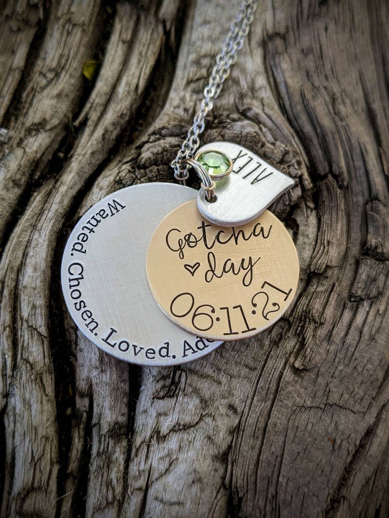 May include: A silver necklace with a silver and gold charm that says "Gotcha day 06:11:21" and a smaller silver charm that says "ALEX".