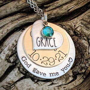 May include: A silver necklace with a layered pendant featuring a heart with the word "GRACE" and the date "10.29.21" on a gold disc. The pendant also includes a teal gemstone and the text "God gave me you."