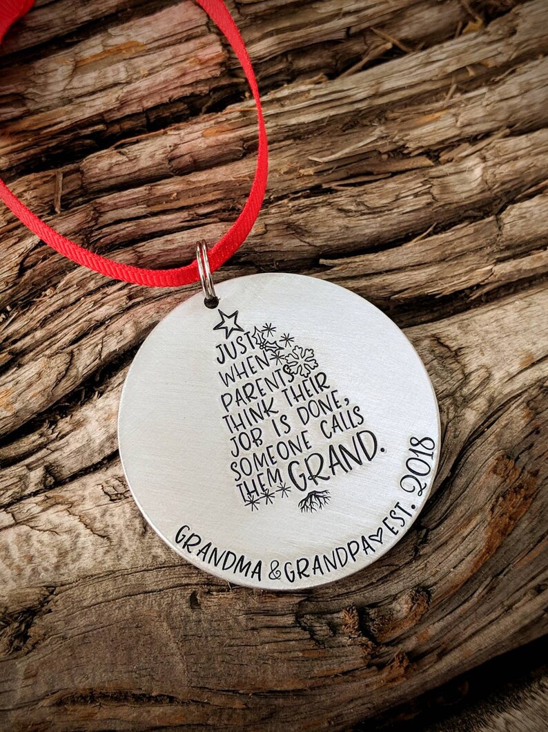 May include: Silver Christmas ornament with a stylized tree design and the text "JUST WHEN PARENTS THINK THEIR JOB IS DONE, SOMEONE CALLS THEM GRAND. GRANDMA & GRANDPA EST. 2018"