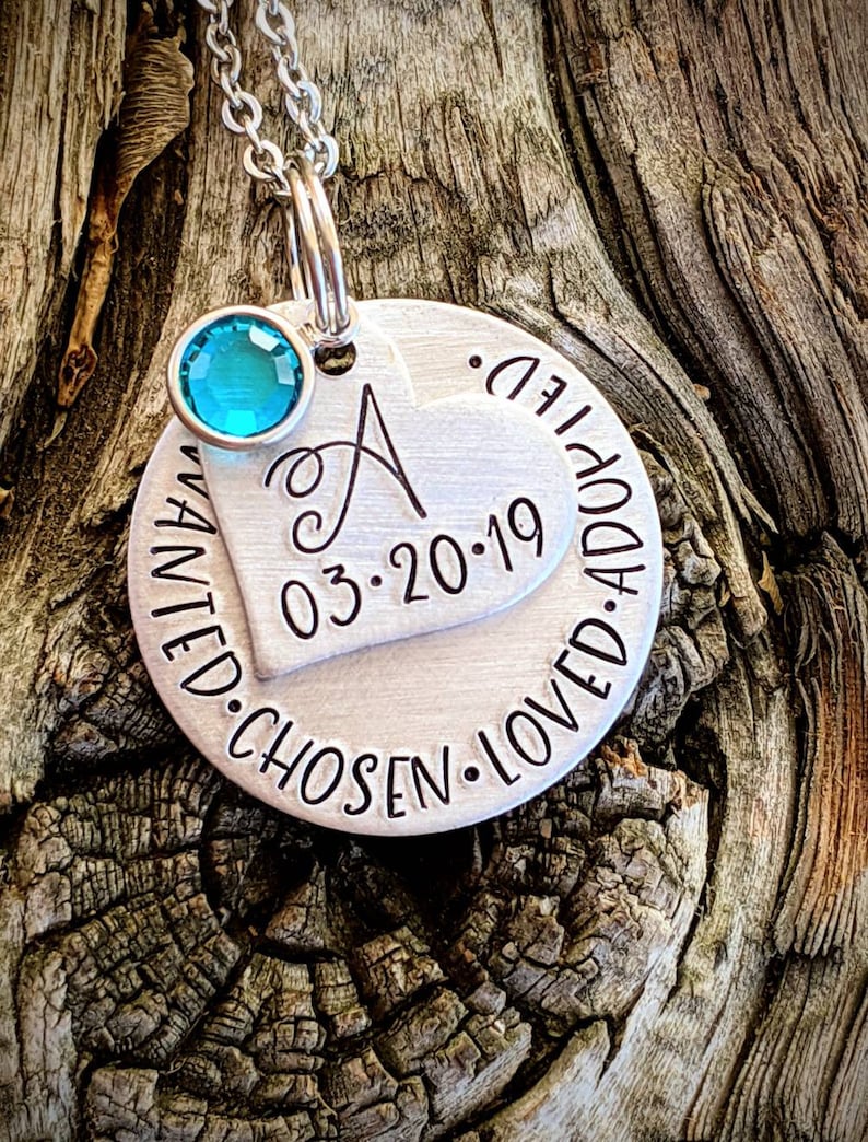 May include: Silver necklace with a round pendant that says "Wanted. Chosen. Loved. Adopted." and a heart charm with the letter "A" and the date "03.20.19". A turquoise gemstone is attached to the necklace.