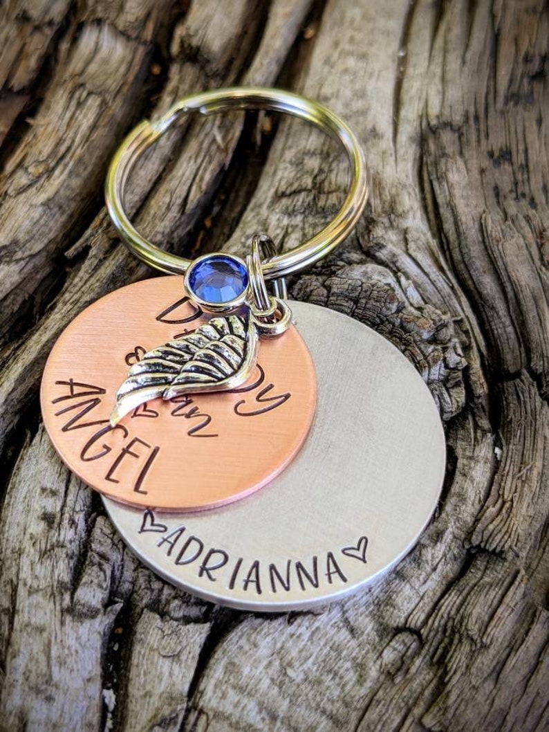May include: Copper and silver keychain with a blue rhinestone, a small silver wing charm, and the text "My Angel is in Heaven" and "Adrianna" on the bottom.