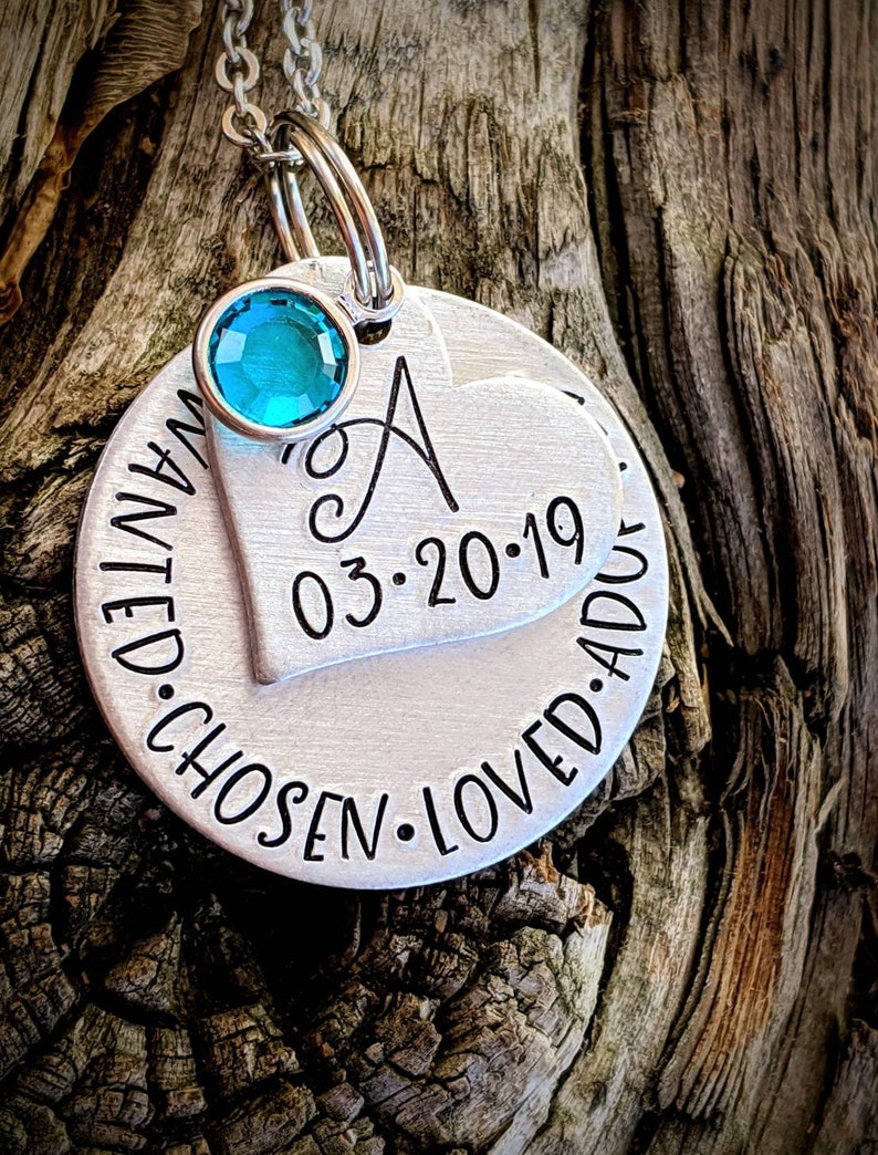 May include: Silver necklace with a heart charm engraved with the letter A, the date 03.20.19, and the words "wanted. chosen. loved. adored". A turquoise blue gemstone is attached to the chain.
