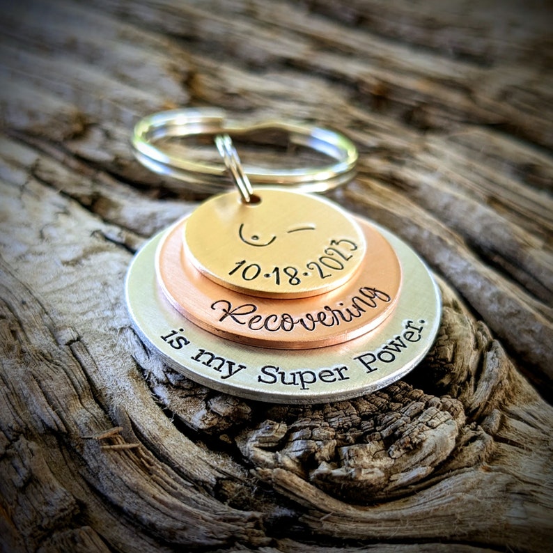 May include: A silver, copper, and gold layered keychain with the text "Recovering is my Super Power." and the date "10-18-2013".