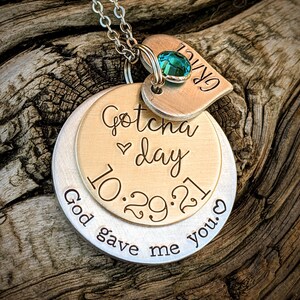 May include: A silver necklace with a heart charm that says "GRACE" and a round charm that says "Gotcha day 10.29.21 God gave me you." The heart charm has a teal blue gemstone.